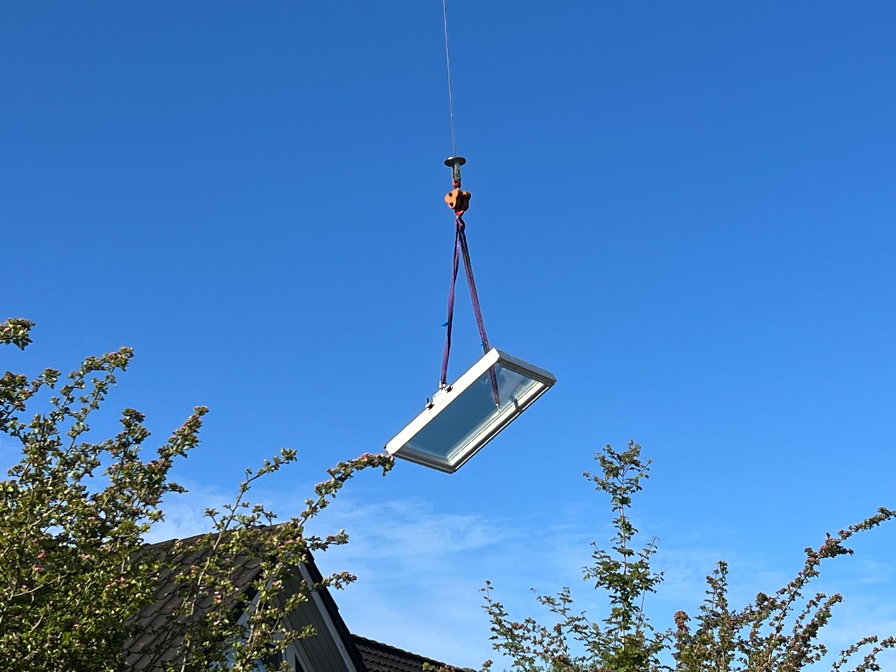 Dachfenster am Kranhaken vor blauem Himmel